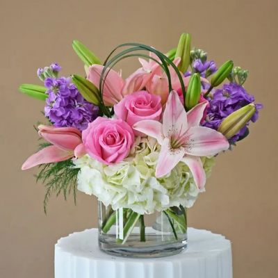 Lavender stock, pink roses, hydrangeas and fragrant lilies in a clear cylinder.