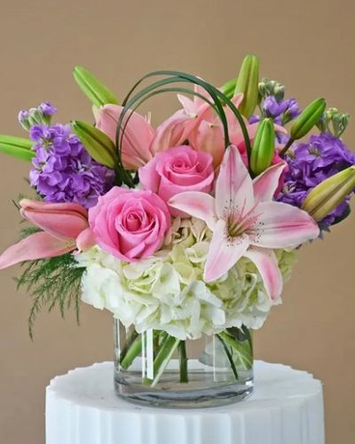 <p>Lavender stock, pink roses, hydrangeas and fragrant lilies in a clear cylinder</p>