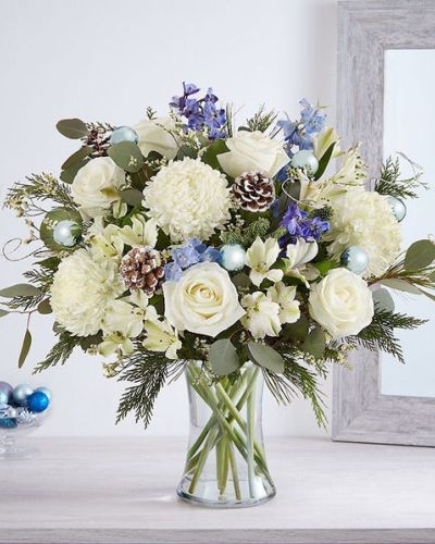 Send wonderful winters wishes with our luxurious arrangement. Snowy white blooms are gathered with lush greenery, accents of blue, gray and glistening silver & gold. Loosely gathered in a glass vase, it’s a gift designed with stunning seasonal style.