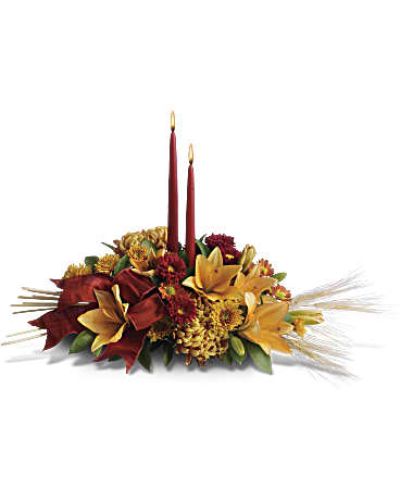 <p>Add a graceful glow to your Thanksgiving dinner table or fall-decorated foyer with this warm, seasonal arrangement. Lilies, mums and asters are accented with sprays of wheat below glowing taper candles.<br />
This classic Thanksgiving centerpiece features orange asiatic lilies, red matsumoto asters, bronze disbud mums, bronze daisies and bronze cushion mums.<br />
Burgundy satin ribbon, stems of wheat, and two taper candles add seasonal sophistication.</p>