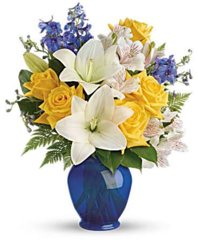 Like a sunny day at the shore, this bright bouquet invigorates and inspires! Radiant yellow roses, white lilies and blue delphinium are expertly arranged in our bold blue plastic ginger jar.
Sunny yellow roses, white asiatic lilies, white alstroemeria, and blue delphinium are arranged with leatherleaf fern and lemon leaf.